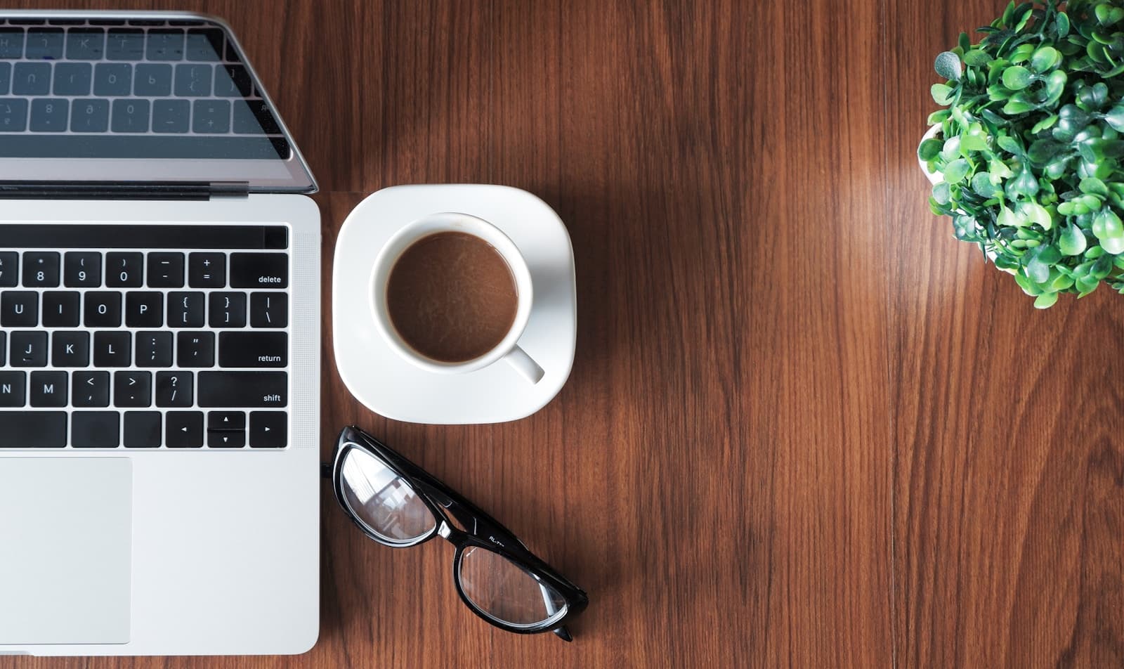 A laptop, coffee, and glasses on a wooden desk