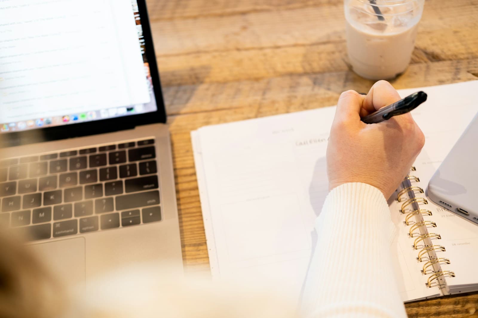 A hand writing in a notebook next to a laptop